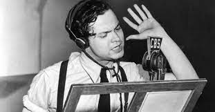Orson Welles in front of the microphone, with raised hand, reading War of the Worlds